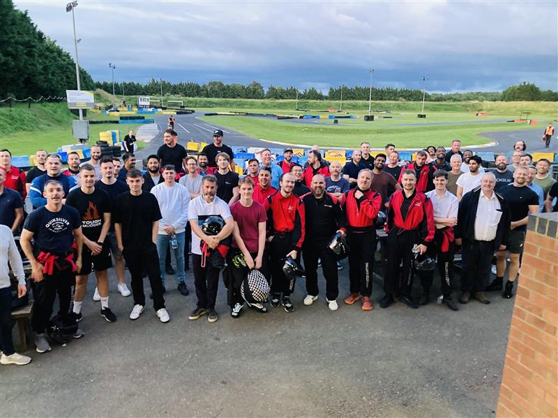 Large group of people stood together on the edge of a gokarting race track